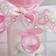 a pink pacifier hanging from a ribbon on top of a white bottle with candy in it