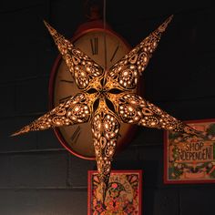 a lighted star hanging from the side of a wall next to pictures and a clock