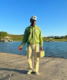 a man standing in front of a body of water wearing a green jacket and tan pants