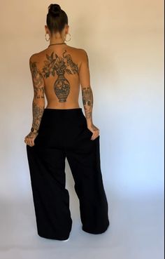 a woman with tattoos on her back standing in front of a white wall and wearing black pants