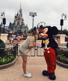 a woman standing next to a mickey mouse in front of a castle with people on it