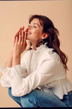 a woman sitting on the ground with her hands clasped to her face and looking up