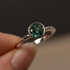 a close up of a person holding a ring with a green gemstone in it