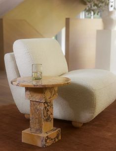 a marble table with a glass on it in front of a white chair and stairs