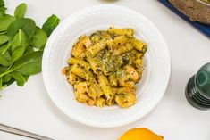 a white plate topped with pasta and spinach next to a bowl of pesto