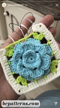 a crocheted square with a flower in the middle is being held by someone's hand