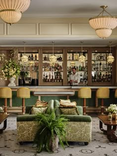 a bar with green couches and chairs in front of it, surrounded by gold chandeliers