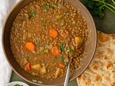 a bowl filled with lentils and carrots next to pita bread