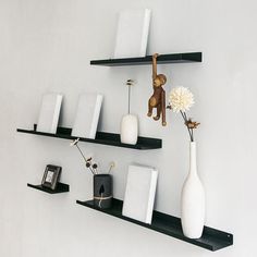 two black shelves with white vases and other items on them in front of a white wall