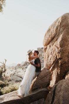 a bride and groom are sitting on rocks in the desert with their arms around each other