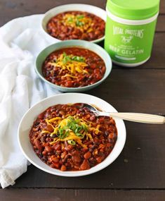 two bowls filled with chili and cheese on top of a wooden table next to a can