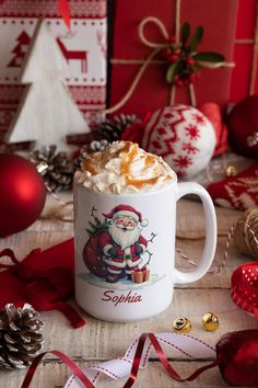 a cup of hot chocolate with whipped cream and santa clause on it, surrounded by christmas decorations