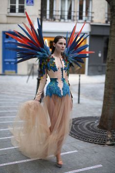 a woman walking down the street wearing a dress with colorful feathers on her head and arms