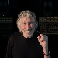 an older man with white hair smiles in front of sound mixing equipment