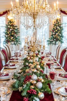 a dining room table decorated for christmas with red and gold decorations, silver candlesticks and greenery