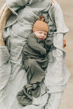 a newborn baby wrapped in a blanket and wearing a brown hat is laying on top of a bed