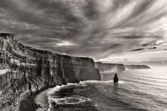 the sun is setting at the edge of an ocean cliff with cliffs in the background