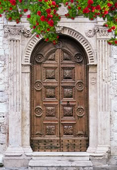 an old wooden door with red flowers growing on it's sides and over the top