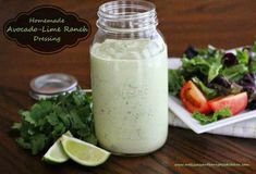 a jar filled with dressing next to a plate of salad and limes on the table