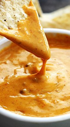 a tortilla chip being dipped into a bowl of quesadilla dip