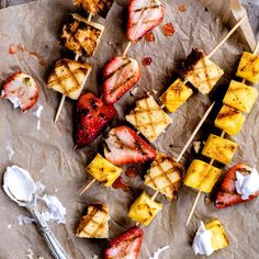 several skewered meats and strawberries on a piece of parchment paper next to a spoon