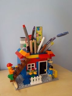 a toy house made out of legos on a table with pens and pencils