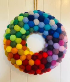 a multicolored felt wreath hanging on a white door with the colors of the rainbow