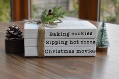 two books sitting on top of a wooden table next to a christmas tree and pine cone