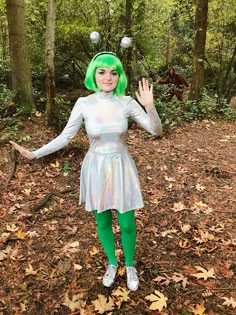 a woman with green hair is standing in the woods holding her hands out and waving