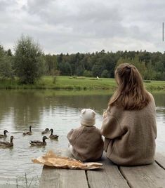 a woman and her child are sitting on a dock watching ducks in the water,