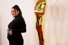 a pregnant woman standing in front of an oscar statue