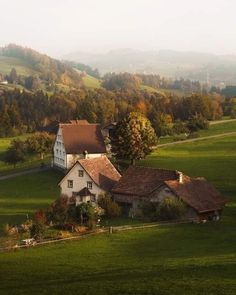 an aerial view of a house in the middle of a green field with trees and hills behind it