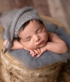 a newborn baby wearing a gray hat is sleeping on a wooden basket with his hands under his chin