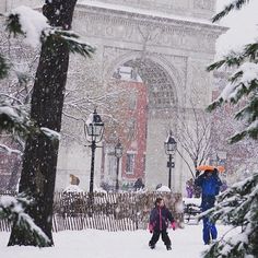 two people walking through the snow in front of a building with an arch on it