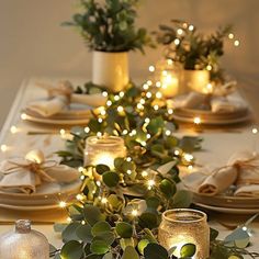 the table is set with candles, plates and vases filled with greenery on it