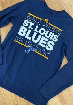 the st louis blues long - sleeved tee shirt is laying on top of a wooden floor