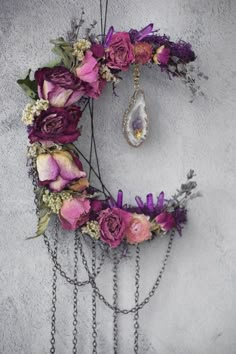 a wreath with flowers and chains hanging from it's sides on the wall next to a necklace