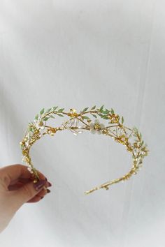 a hand holding a gold tiara with leaves and pearls on it's side