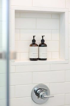 two bottles of hand soap sitting on top of a white shelf next to a mirror