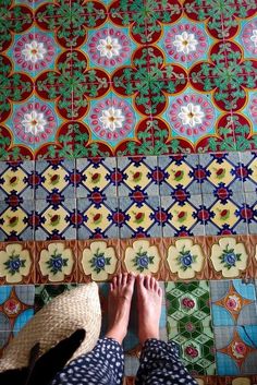 the person is standing in front of a colorful tile wall with their feet up on it