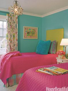 two beds in a room with blue walls and pink bedding, one has a chandelier hanging from the ceiling