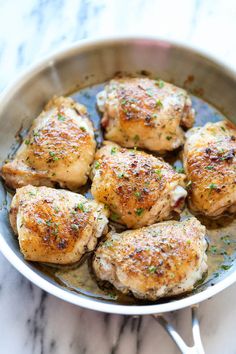 chicken thighs in a skillet on a marble counter top with herbs and seasoning