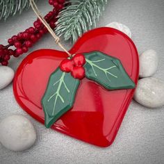 a red heart shaped ornament with holly on it