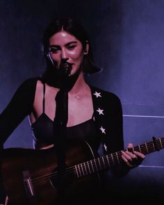 a woman singing into a microphone while holding a guitar