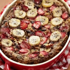 a red casserole dish with bananas and strawberries in it on a checkered cloth