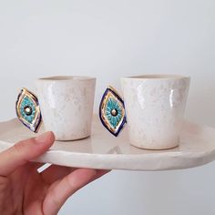 two white cups with blue and green designs on them are sitting on a small plate