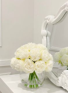 a vase with white flowers sitting on a table in front of a mirror and an ornate chair