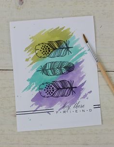 a card with watercolor feathers on it next to a paintbrush and some pencils