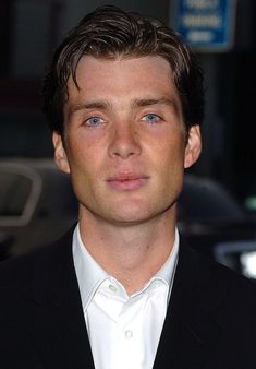 a close up of a person wearing a suit and tie with cars in the background