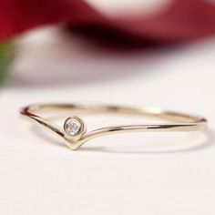 a diamond ring sitting on top of a white surface next to a red rose with petals in the background